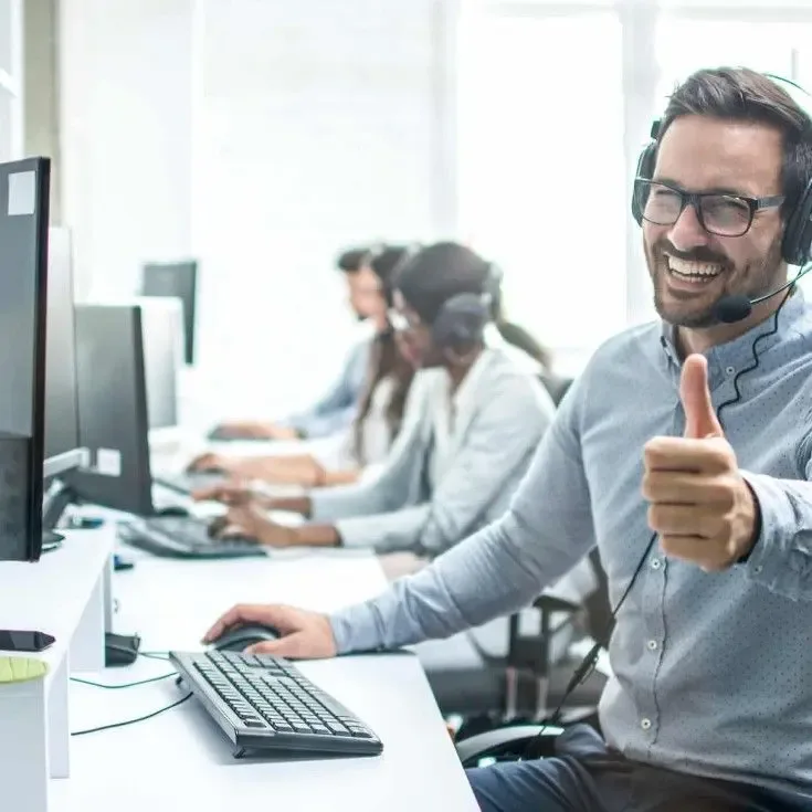 Smiling agent providing call center service with headset in a customer support office, showing positive engagement and satisfaction.
