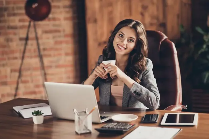 Professional woman working in a cozy back office environment with coffee in hand, showcasing a stress-free atmosphere enabled by back office outsourcing.

