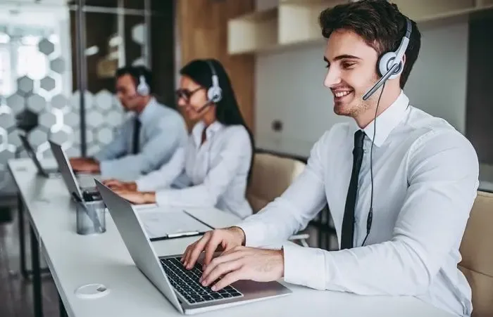 Team of professional agents working at call centres, wearing headsets and assisting customers through laptops in a modern office environment.
