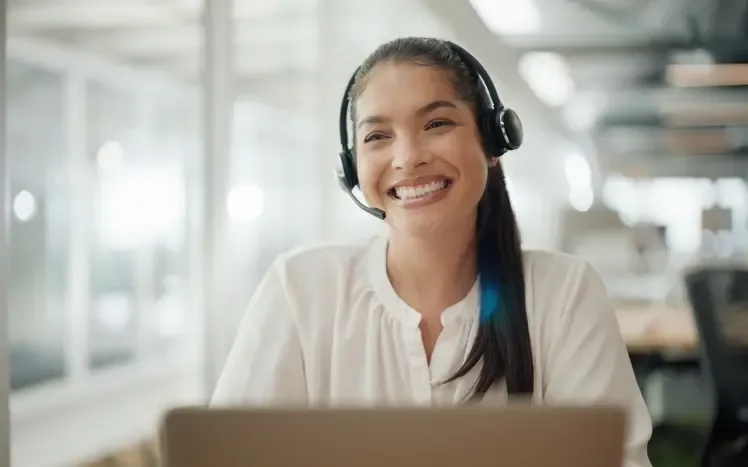 Woman working in a call center at night, smiling and listening to a customer through a VOIP headset at her computer — representing dedicated customer care service and professional support.