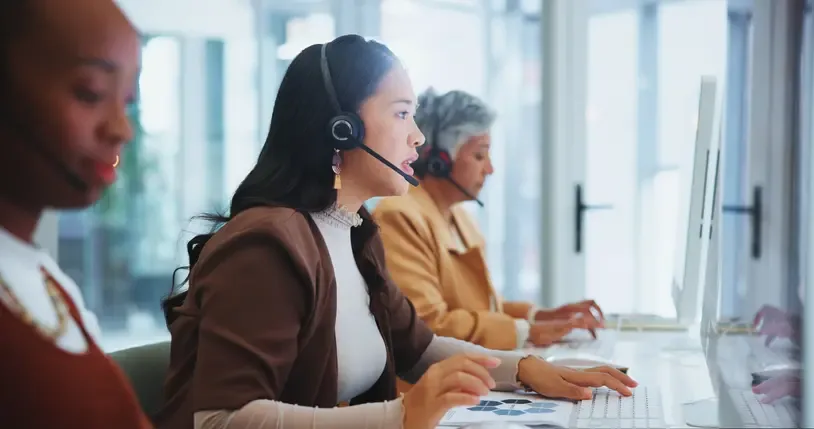 Woman in a call centre wearing headphones, providing client support and online sales assistance — representing customer support via SMS, telemarketing, and virtual customer care solutions.
