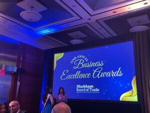 With dim, beautiful lighting, a video screen shows a placeholder image for the Markham Annual Business Excellence Awards ceremony while all invitees wait for the introductory address provided by Markham's mayor, Frank Scarpitti.
