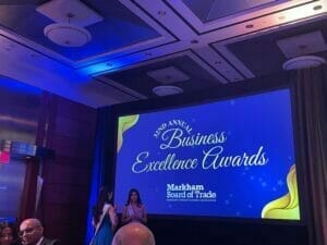 With dim, beautiful lighting, a video screen shows a placeholder image for the Markham Annual Business Excellence Awards ceremony while all invitees wait for the introductory address provided by Markham
