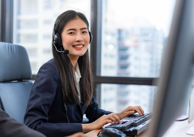 A beautiful, smiling female Japanese speaking Big Tech outsourcing technical support rep works on her computer, ensuring superb customer support via live chat for a Forex trading platform.
