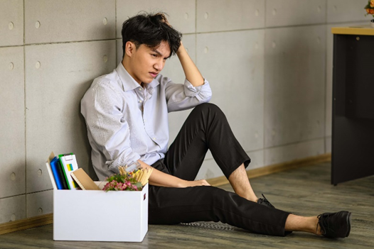 A depressed man has slumped down to the ground because they were forced to resign from their position as a customer service representative. This shows the extreme importance knowing how to decrease employee attrition rates.
